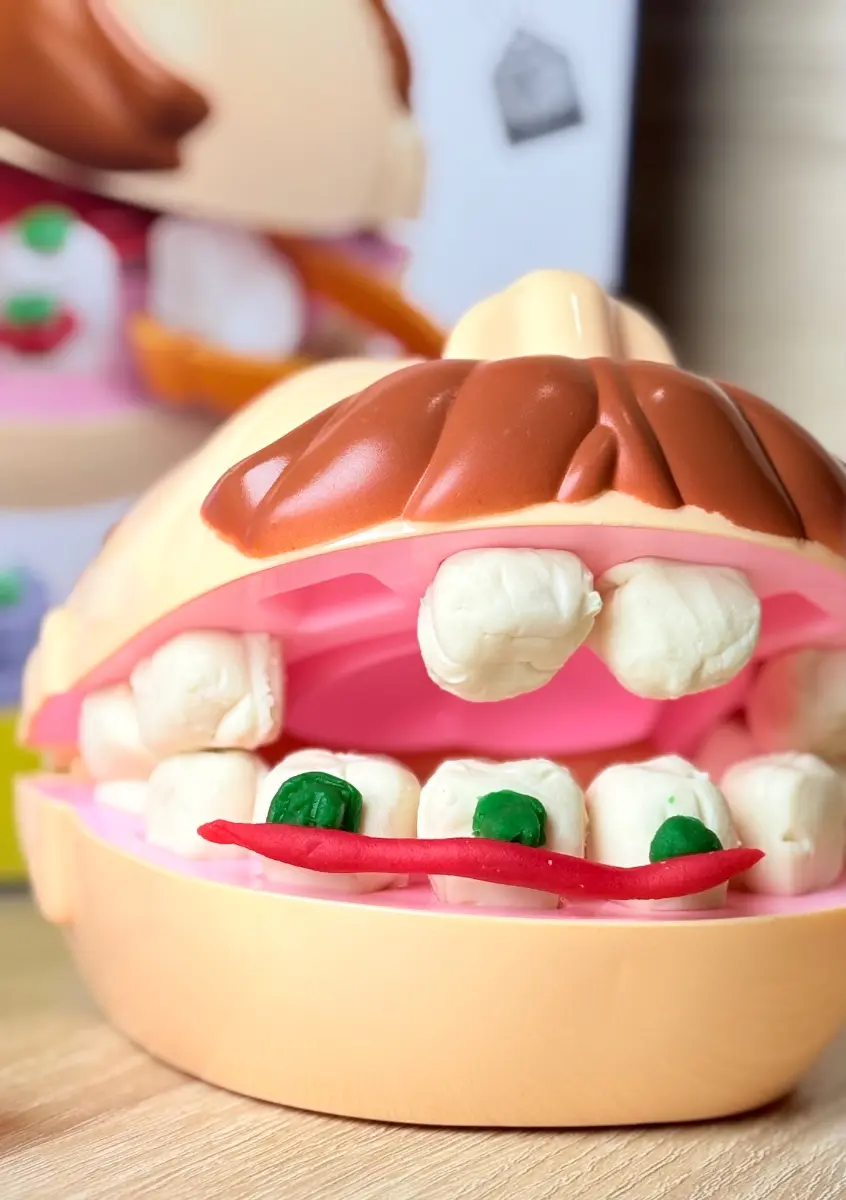 Modelo de dentadura didáctica infantil en plástico beige con dientes y lengua de masa moldeable que simula caries con manchas verdes.