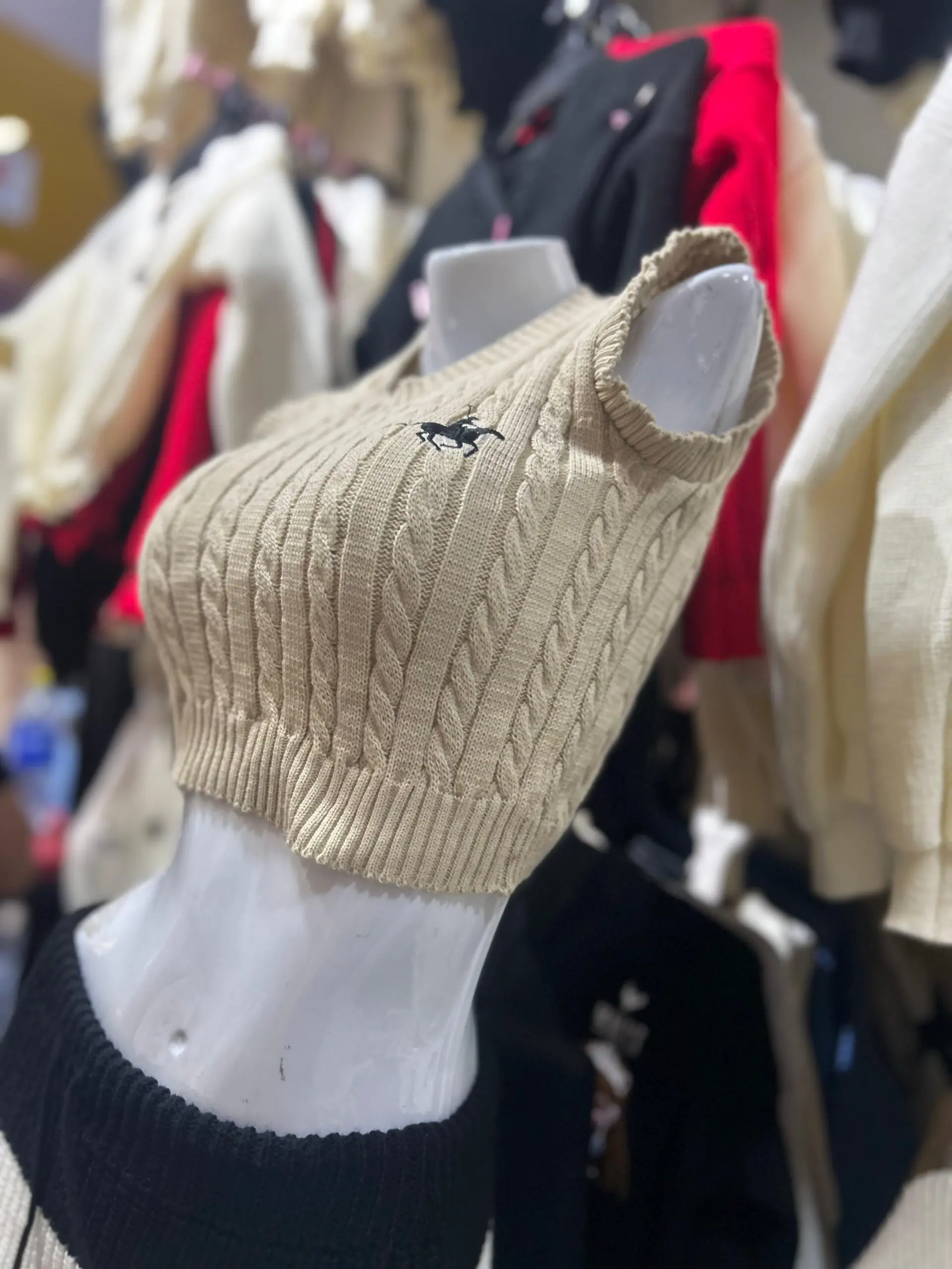 Top tejido sin mangas color café con textura de trenzas, cuello en V y pequeño logo frontal, exhibido en maniquí blanco.