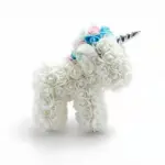 Unicornio de rosas eternas blancas con crin de rosas azules y rosadas, cuerno plateado y oreja con brillo, visto de perfil.