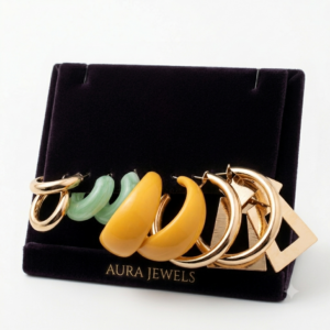 Cinco pares de candongas en tonos dorados, verde menta y amarillo, dispuestos sobre un soporte de terciopelo oscuro de Aura Jewels.