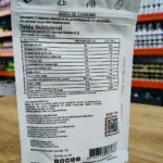Reverso de empaque plateado de Vitamina D3 K2 con tabla nutricional, modo de consumo e ingredientes sobre una mesa de madera.