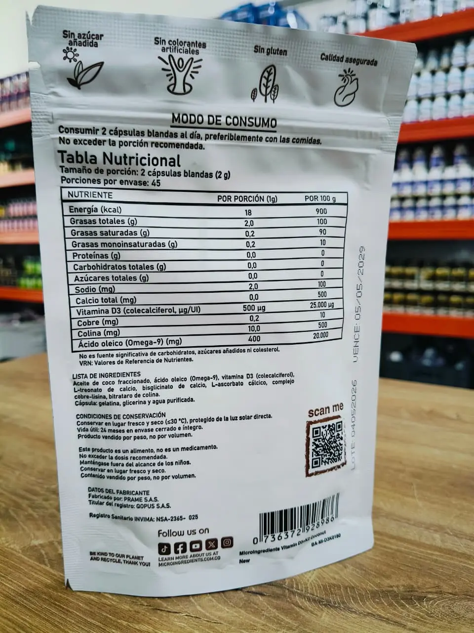 Reverso de empaque plateado de Vitamina D3 K2 con tabla nutricional, modo de consumo e ingredientes sobre una mesa de madera.