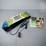 Kit de masajeador Vibratone con maletín blanco y azul, control remoto, aplicador negro y manuales de uso sobre fondo gris.