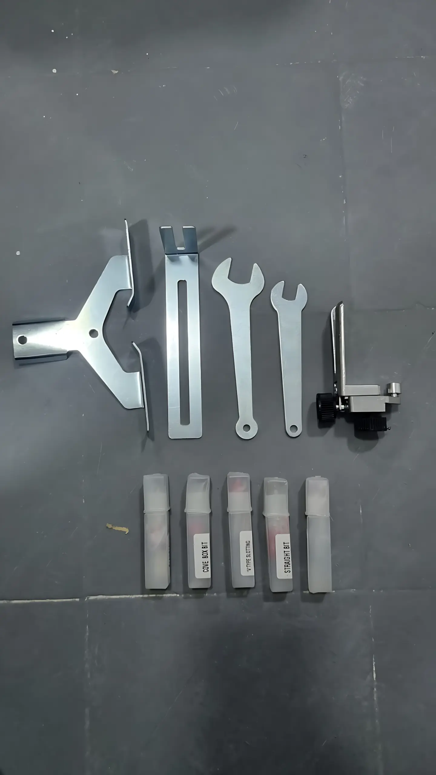 Kit de accesorios para recortadora de madera metálica con base de soporte, dos llaves, guía ajustable y cinco fresas en sus estuches plásticos.