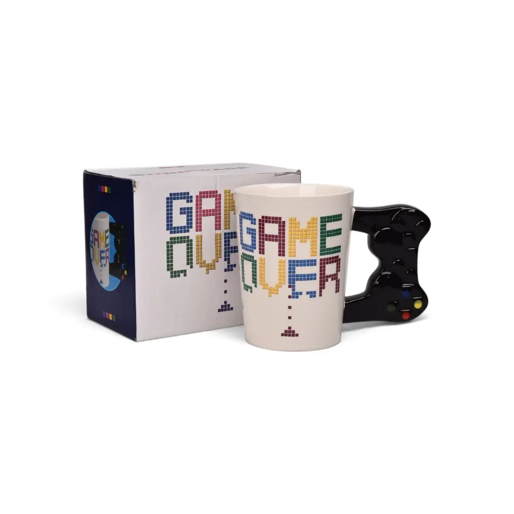 Taza de cerámica blanca con diseño multicolor de pixeles y frase Game Over, con asa en forma de control de videojuegos negro, junto a su caja de empaque.