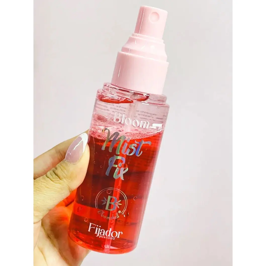Mano sosteniendo spray fijador Bloomshell Mist Fix con líquido rojo y atomizador rosa para refrescar la piel y prolongar el maquillaje.