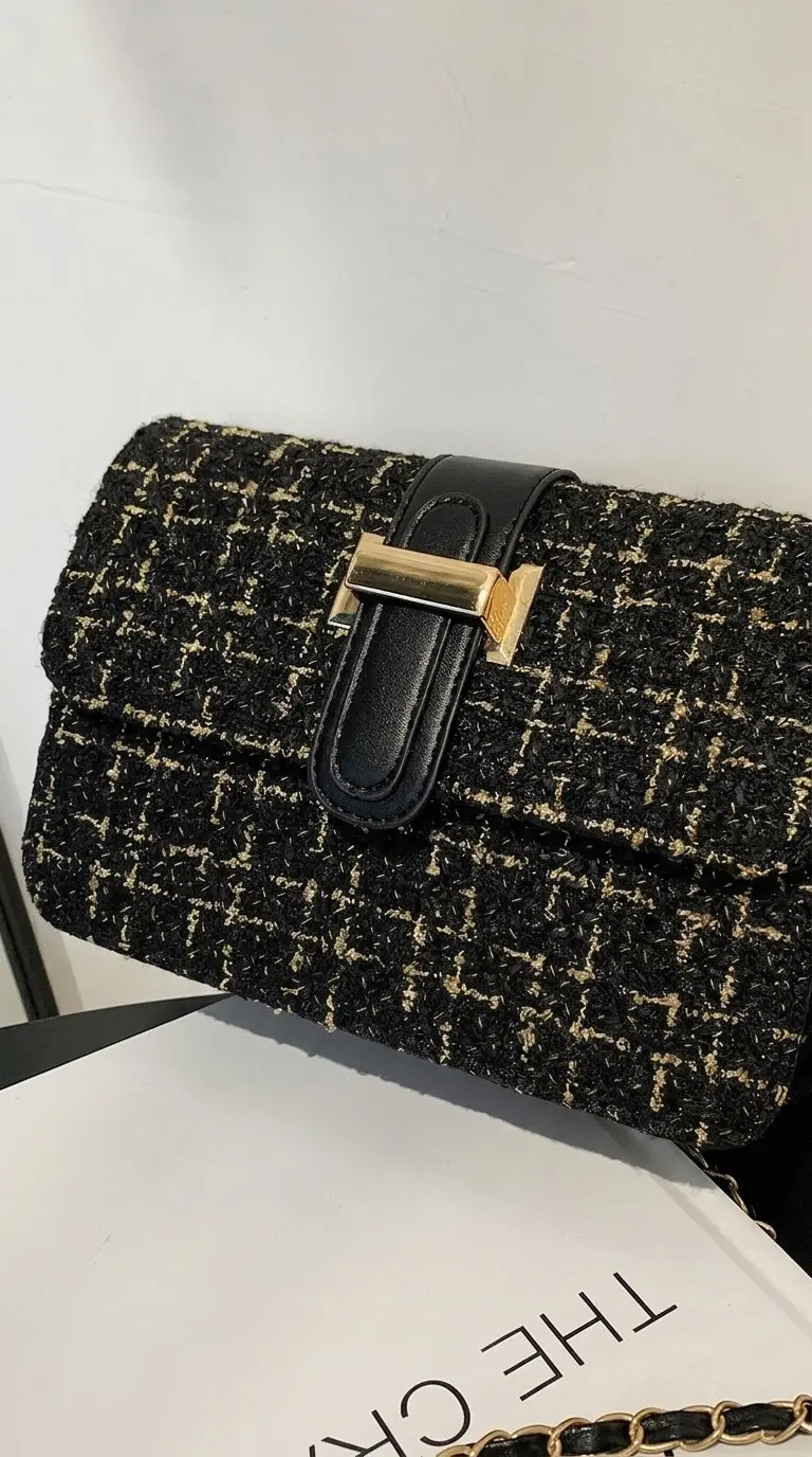 Bolso de mano negro y dorado en tweed texturizado con solapa, cierre de lengüeta sintética y herrajes metálicos.