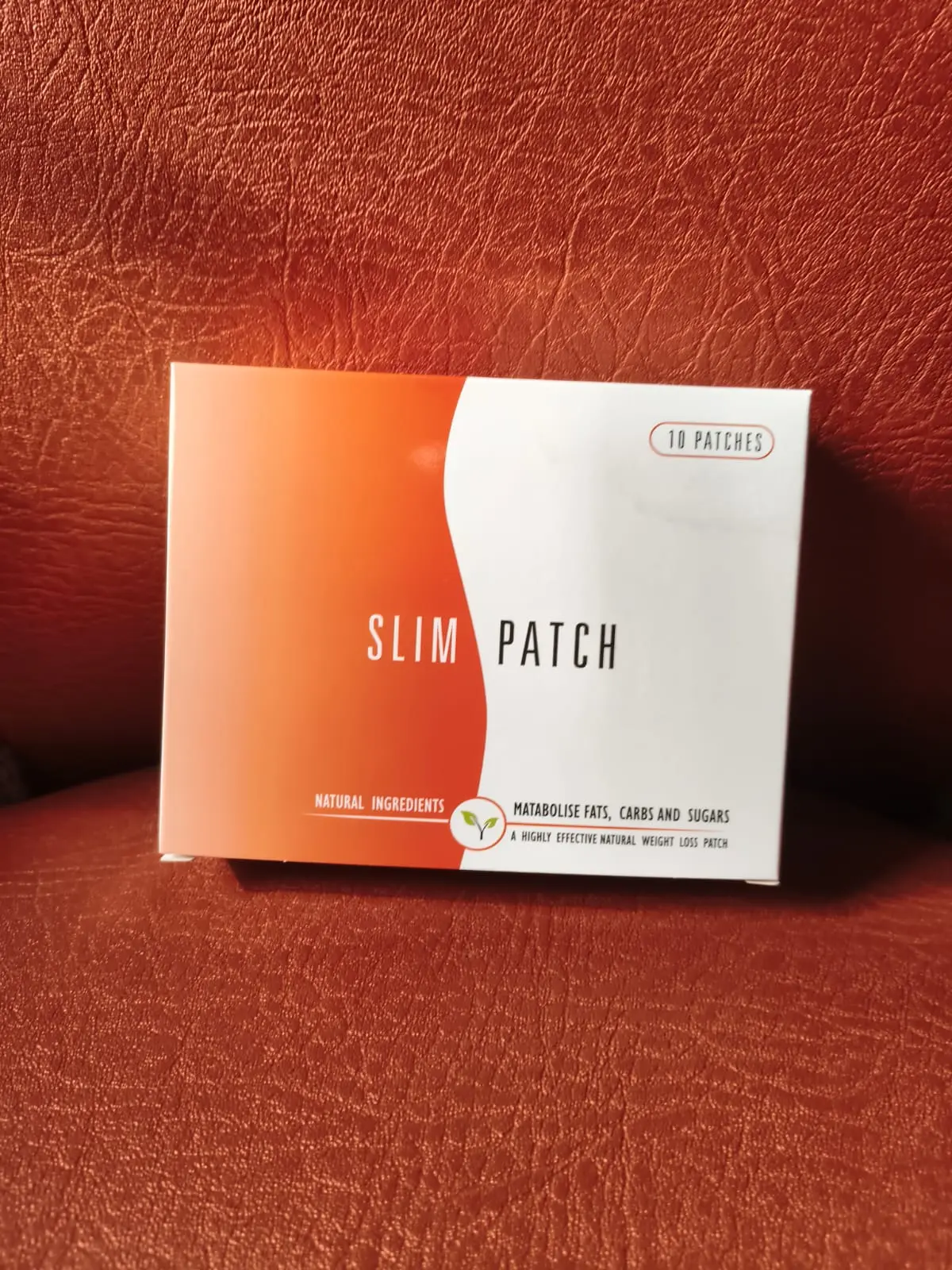 Caja blanca y naranja de parches reductores corporales naturales para definir la silueta, sobre fondo de cuero texturizado.