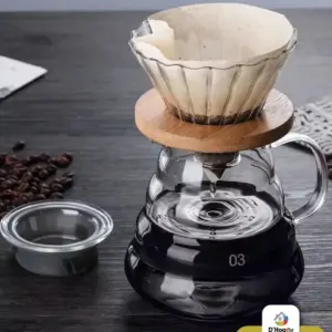 Cafetera V60 de vidrio borosilicato con base de bambú, jarra con café y tapa de vidrio sobre mesa oscura con granos de café.