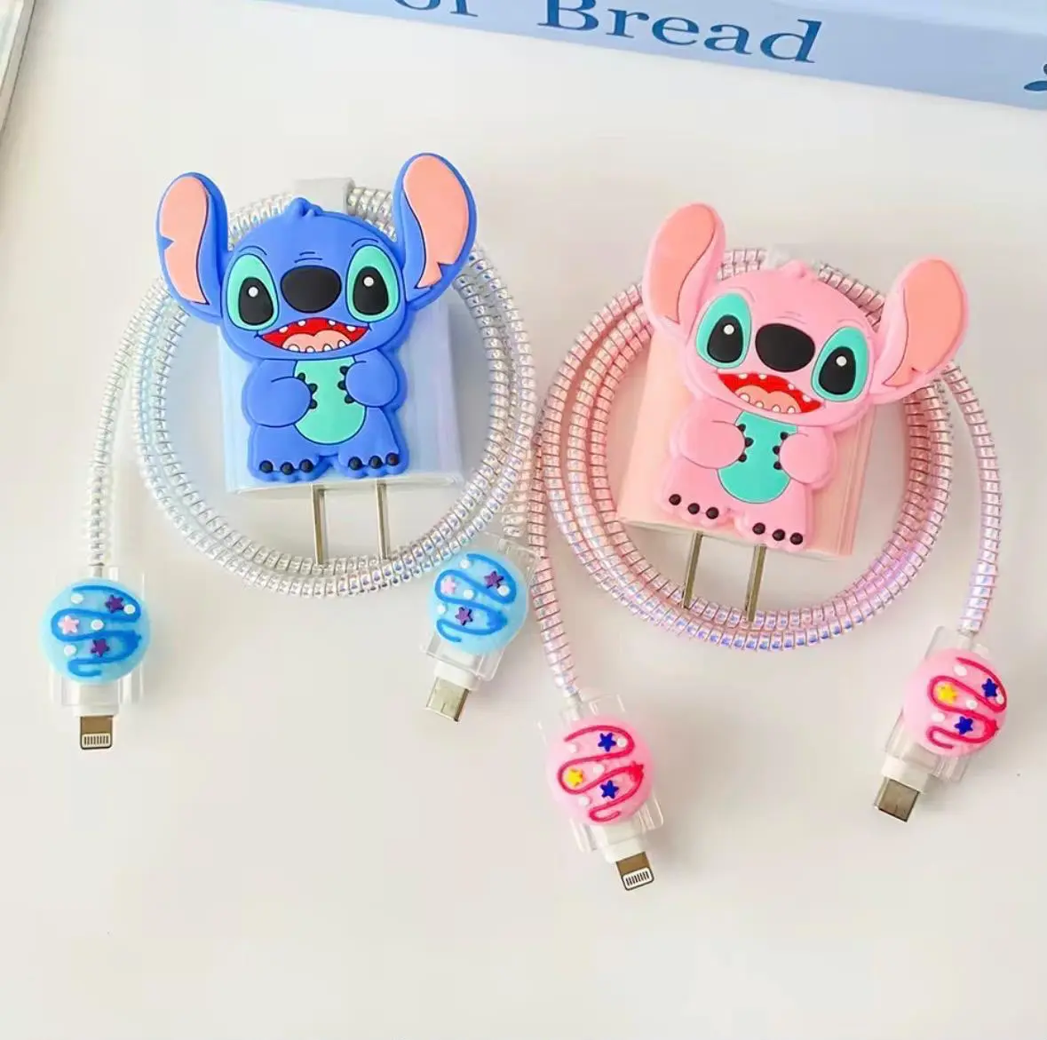 Dos protectores de silicona para cargador con diseño de Stitch en azul y rosa, incluyen espirales para cables y figuras decorativas para los conectores.