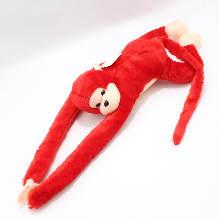 Peluche de mono rojo con extremidades largas y flexibles, cara y pies beige, textura suave y esponjosa sobre fondo blanco.