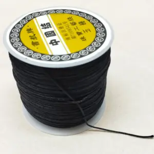 Bobina de hilo coreano negro resistente para bisutería, con etiqueta amarilla en la parte superior y un extremo suelto sobre superficie blanca.