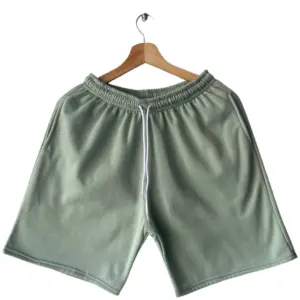 Pantaloneta deportiva de algodón verde manzana para hombre con cordón blanco y bolsillos, colgada en gancho de madera.