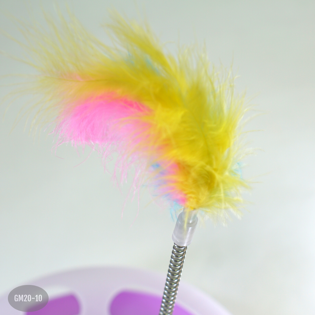 Juguete interactivo para gatos con resorte metálico flexible, base circular morada y plumas coloridas en tonos amarillo, rosado y azul.