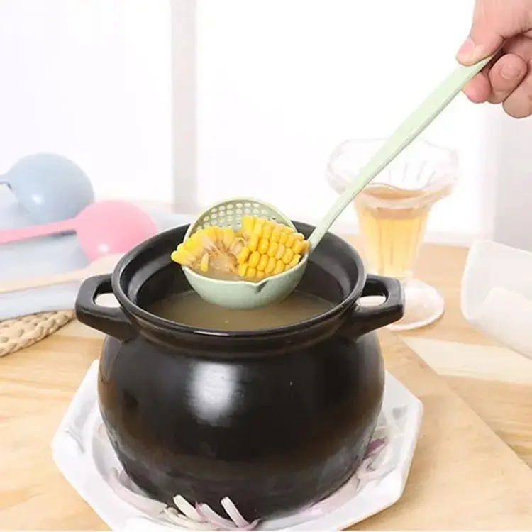Cucharón con colador integrado color verde claro sacando maíz de una olla negra con caldo, diseñado para separar sólidos de líquidos al servir.