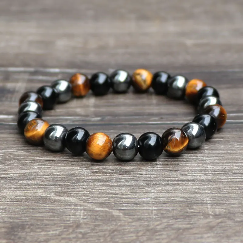 Pulsera de protección con cuentas esféricas de ojo de tigre, obsidiana negra y hematita metálica dispuestas en patrón alternado sobre superficie de madera.
