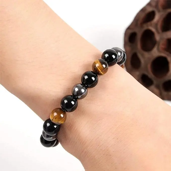 Pulsera de protección con cuentas esféricas de obsidiana negra, hematita metálica y ojo de tigre marrón, ajustada en una muñeca sobre fondo blanco.