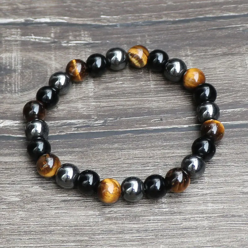 Pulsera de protección con cuentas esféricas de ojo de tigre, hematita metálica y obsidiana negra dispuestas en patrón circular sobre superficie de madera.