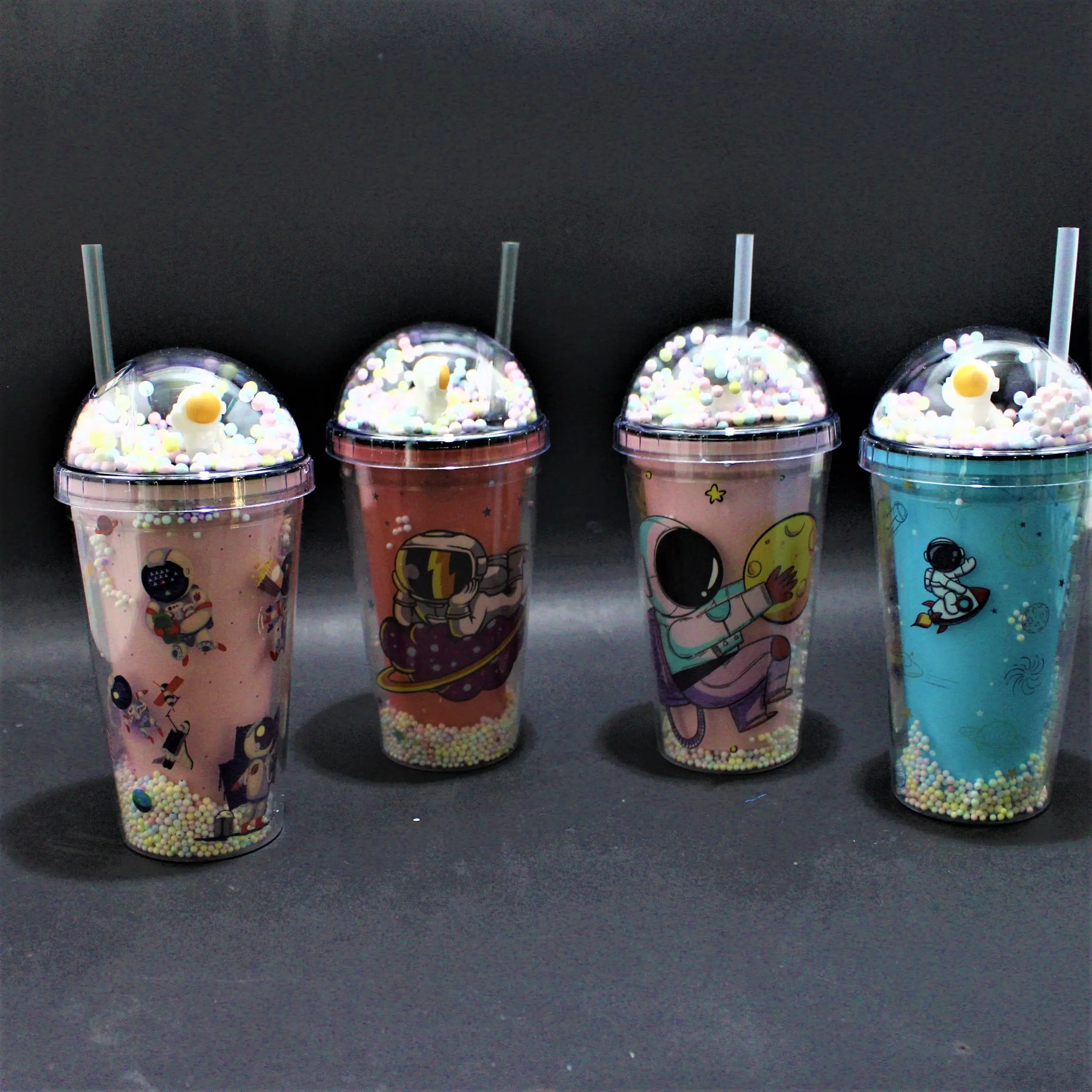 Set de cuatro termos plásticos transparentes con tapa abovedada, relleno de bolitas de colores, pitillo y diseños espaciales de astronautas.