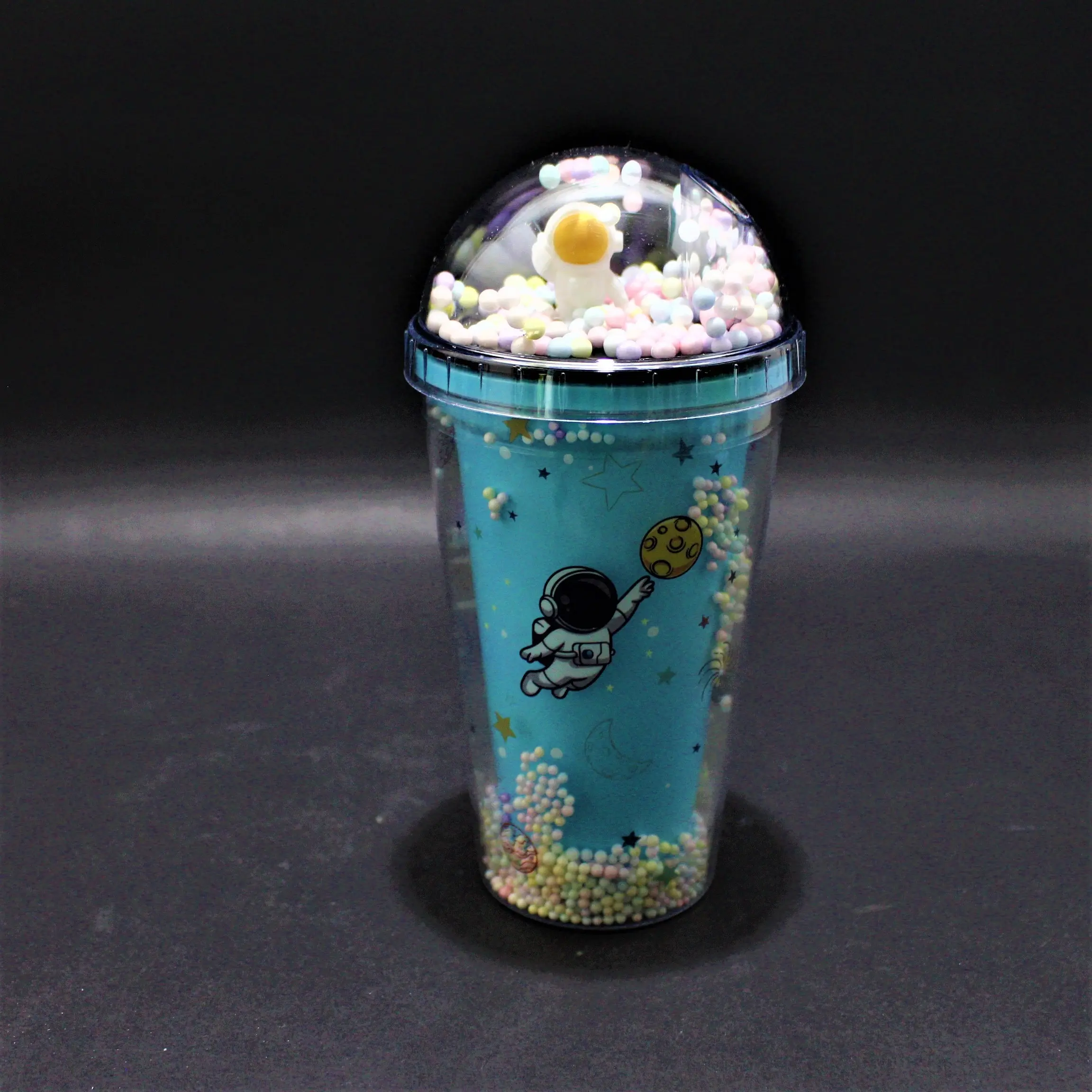 Termo azul con estampado de astronauta y tapa domo transparente llena de pequeñas esferas de colores y figura de astronauta en relieve.