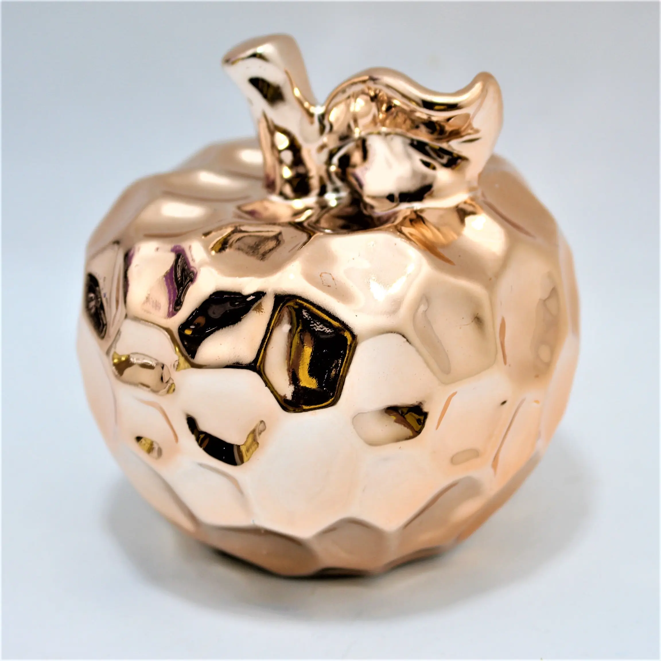 Manzana decorativa pequeña de cerámica con acabado metálico dorado brillante y diseño facetado.