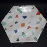 Paquete de platos desechables hexagonales blancos con diseño multicolor estilo terrazo y destellos dorados para fiestas.
