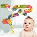 Set de toboganes de agua multicolor con ventosas y patitos amarillos, instalado en la pared para baño infantil, junto a un bebé sonriente.