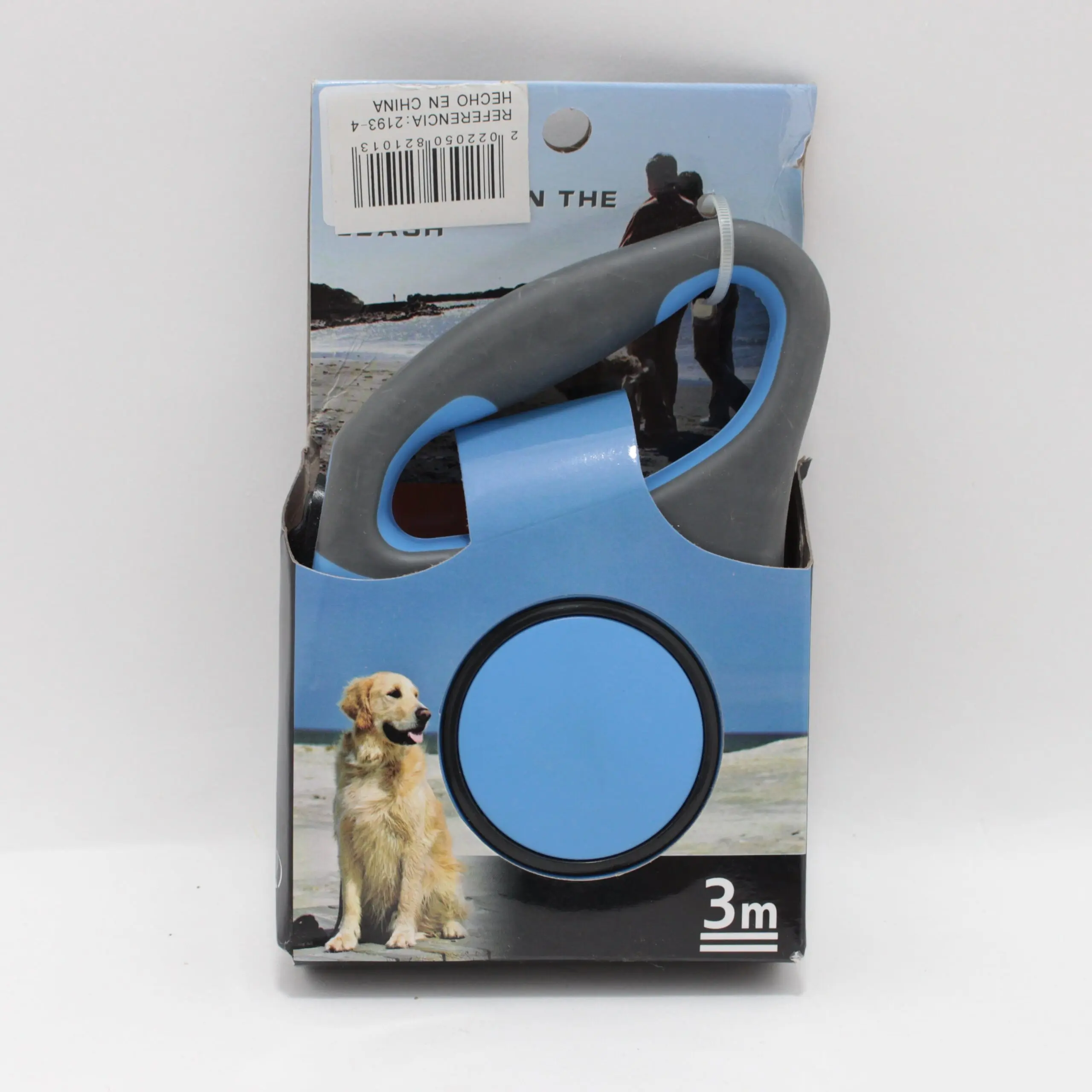 Correa retráctil para perro de 3 metros azul y gris en su caja de presentación con de Golden Retriever en la playa.