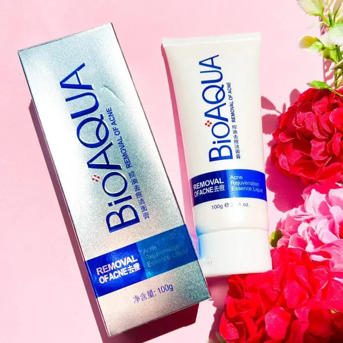Set de jabón antiacné Bioaqua 100g en tubo blanco y caja plateada, con detalles en azul, sobre fondo rosado con flores rojas.