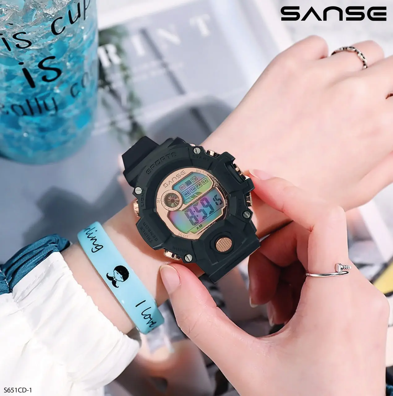 Reloj deportivo digital negro con pantalla multicolor y detalles dorados en la muñeca de una mujer.