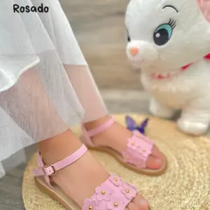 Sandalias planas infantiles color rosado con diseño de flores texturizadas, tira ajustable al tobillo y suela flexible.