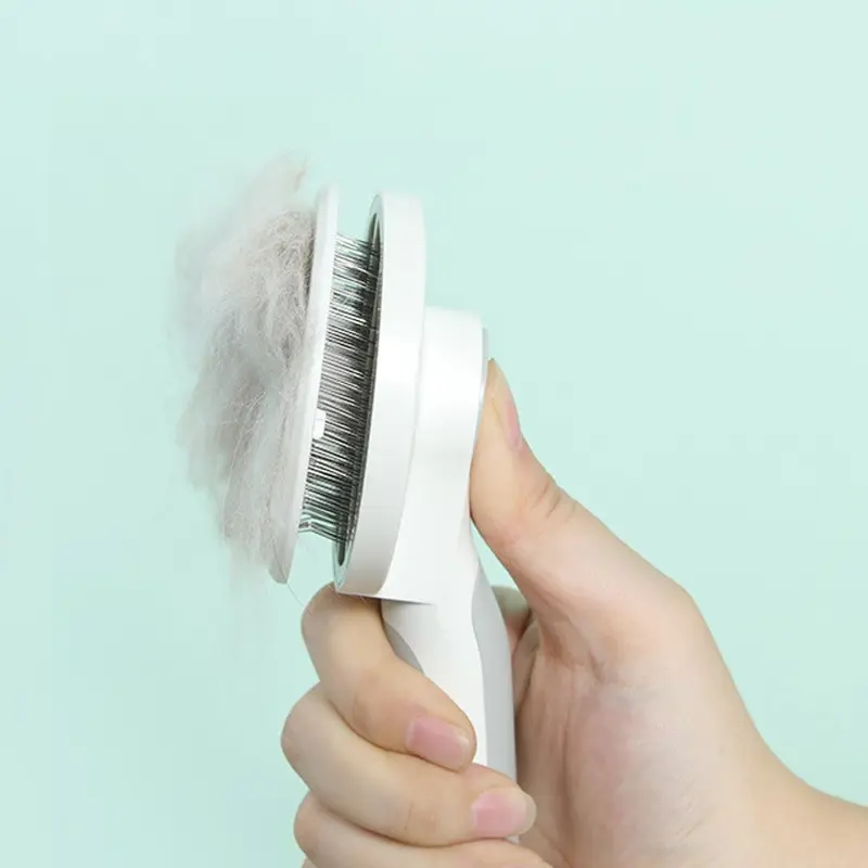 Mano sosteniendo cepillo removedor de pelos blanco con cerdas metálicas y vello gris atrapado sobre fondo verde claro.