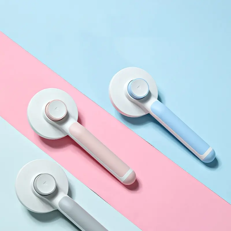 Cepillos autolimpiantes para mascotas en colores azul, rosado y gris, con mango ergonómico y botón central, dispuestos sobre fondo bicolor.