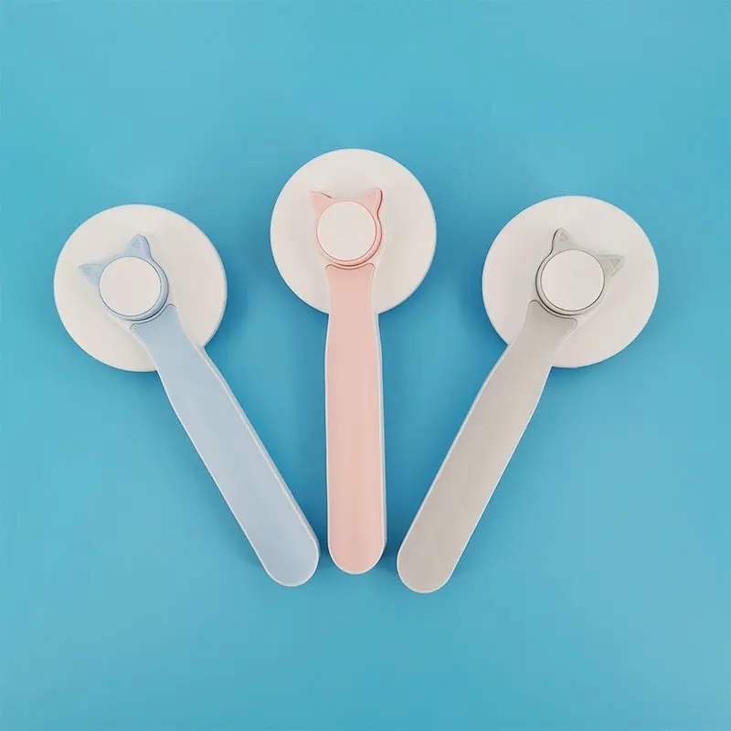 Tres cepillos para mascotas con diseño de gato, en colores azul, rosado y gris, organizados en abanico sobre fondo azul.