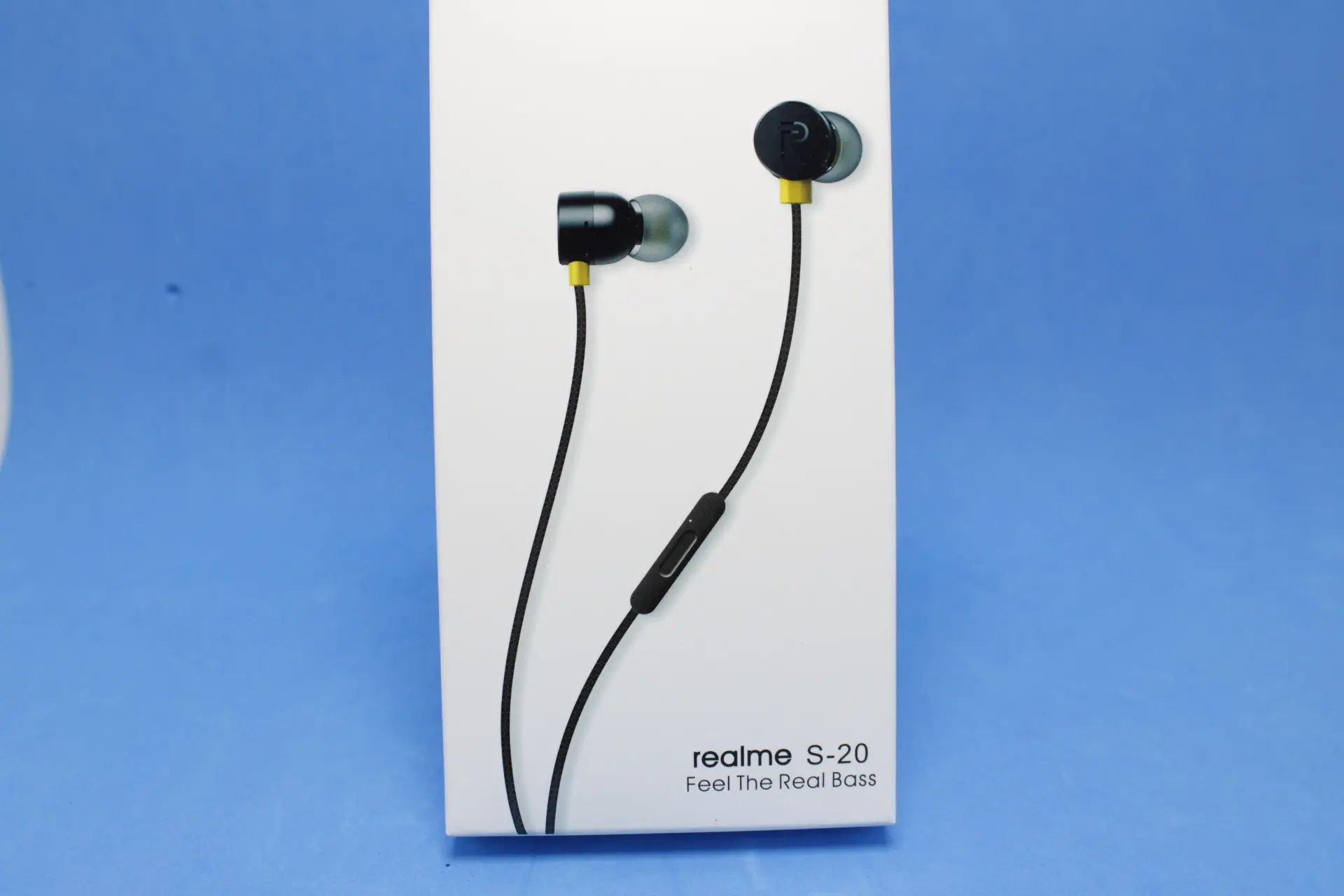 Auriculares intraauditivos Realme S-20 negros con detalles amarillos y micrófono en cable, presentados en empaque blanco sobre fondo azul.
