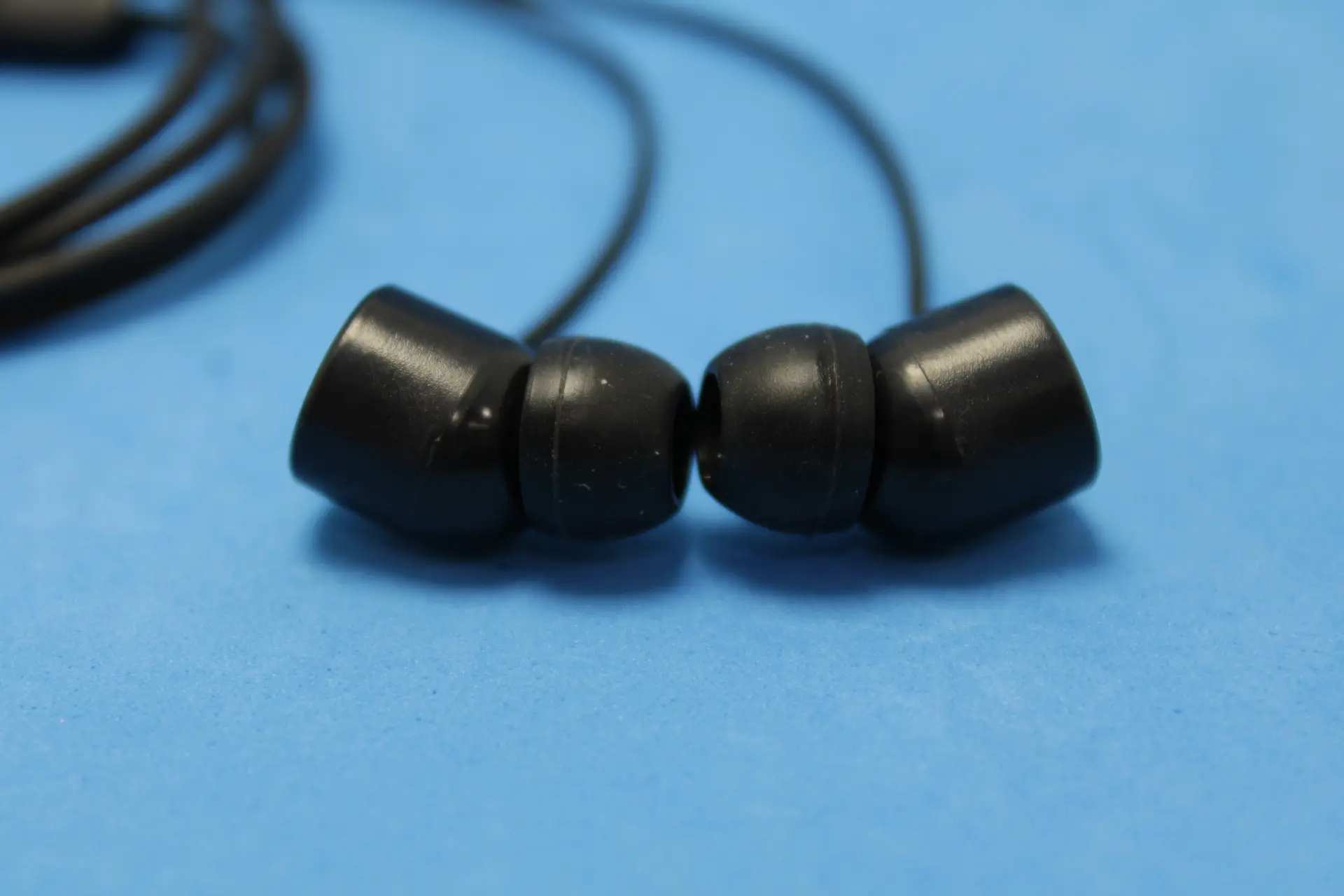 Primer plano de auriculares intraauditivos Realme S-20 negros mate con almohadillas de silicona y cable delgado sobre fondo azul