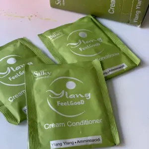 Set de cuatro sobres verdes de crema acondicionador Ylang FeelGood con aminoácidos sobre superficie blanca y caja de empaque abierta.