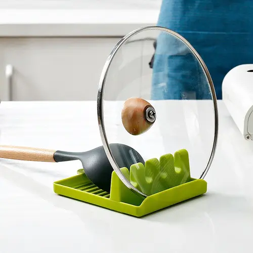 Soporte verde de plástico para cocina con ranuras para organizar tapas de ollas y utensilios, manteniendo la encimera limpia y ordenada.
