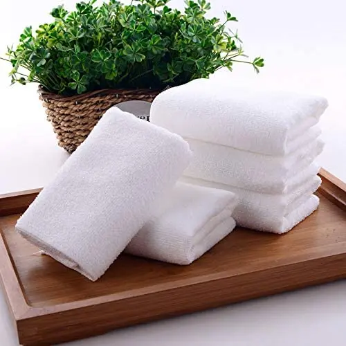 Paños de microfibra blancos multiuso y absorbentes doblados sobre una bandeja de madera, con una planta verde al fondo.
