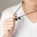 Collar de cordón negro con colgante de mancuerna negra, sostenido por una mano para mostrar su detalle y tamaño sobre una camiseta blanca.