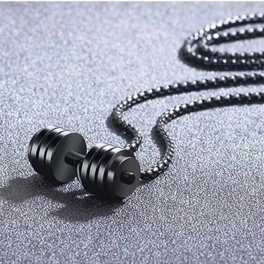 Collar de acero de titanio con colgante de mancuerna negra y cadena de cuentas negras sobre fondo gris texturizado.