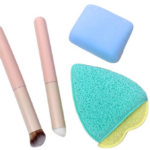 Set de maquillaje con dos brochas de mango rosado, una esponja rectangular azul y un aplicador triangular turquesa y amarillo.