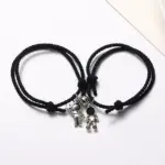 Par de pulseras de cordón negro ajustable con dijes de astronautas plateados y detalles negros, dispuestas juntas sobre fondo blanco.