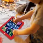 Niño dibuja un astronauta con marcador luminoso sobre una pizarra digital educativa de marco rojo, ideal para aprendizaje creativo y escritura.