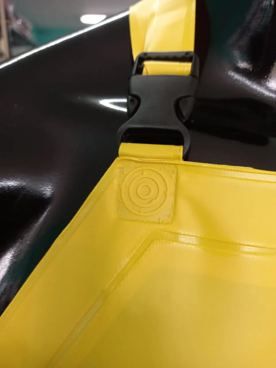 Detalle de hebilla negra de plástico y tirante amarillo en un delantal impermeable de PVC para industria y limpieza.