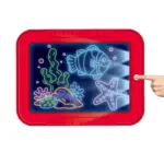 Pizarra digital educativa roja con pantalla iluminada que muestra dibujos de peces y corales, activada por un dedo sobre el botón lateral de encendido.