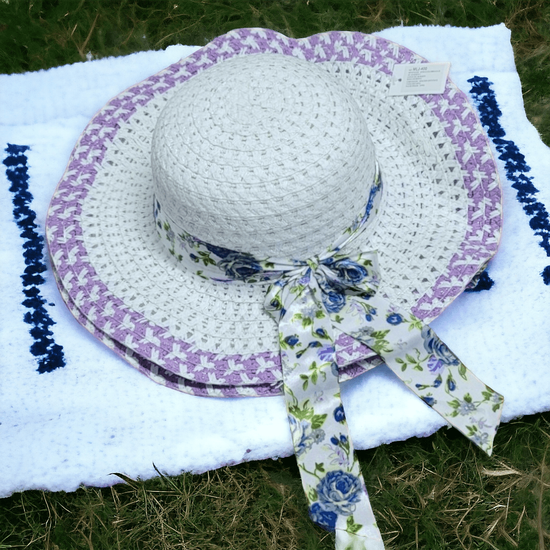 Set x3 sombreros blancos de ala grande con borde morado y lazo estampado floral azul, sobre toalla blanca en césped.