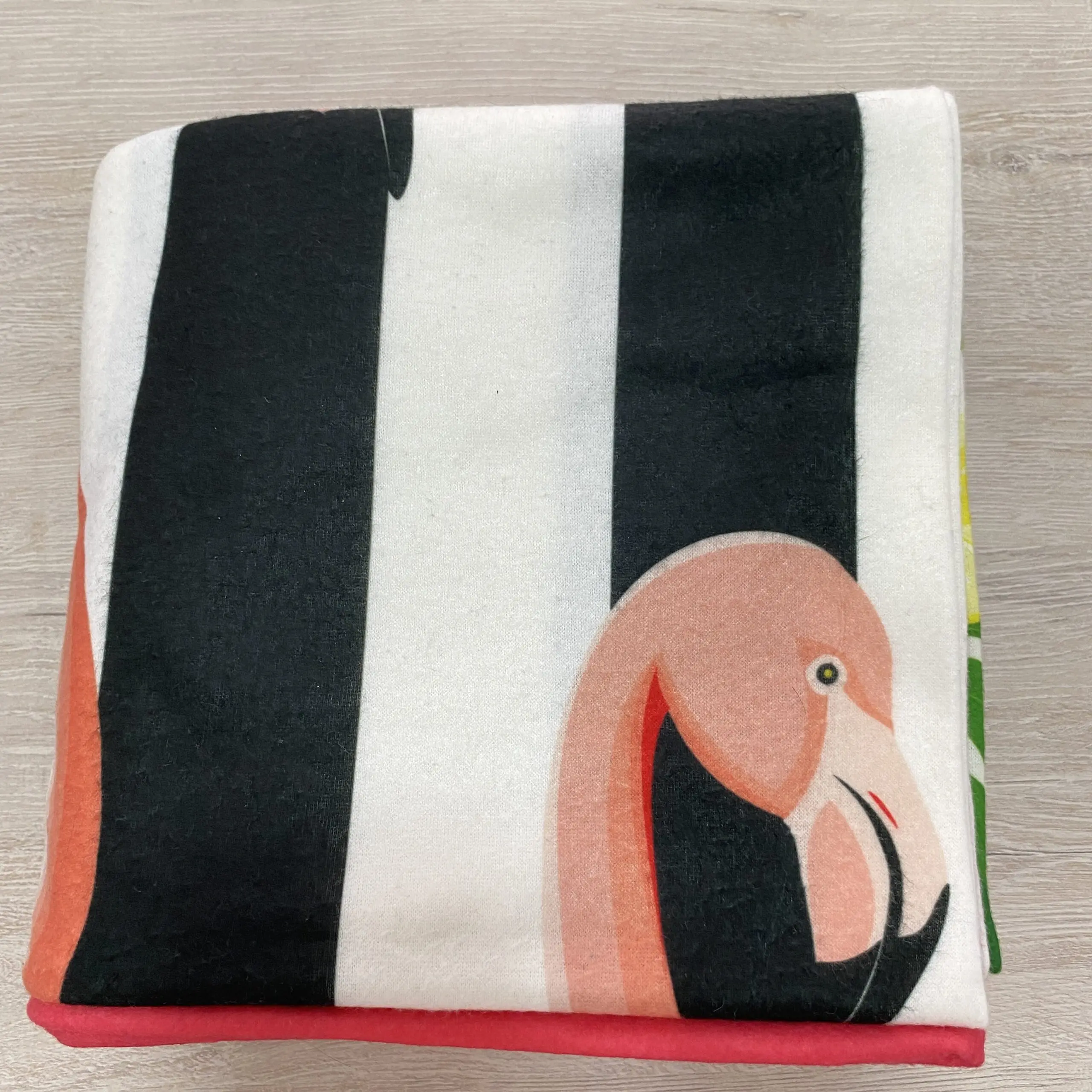 Manta polar fleece Flamingo Shore doblada con diseño tropical de flamenco rosa sobre franjas negras y blancas, suave y con borde rojo.