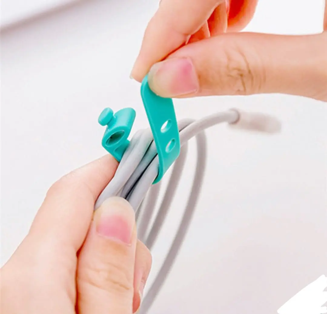 Manos usando un broche organizador de cables de silicona color turquesa para sujetar un cable gris enrollado.