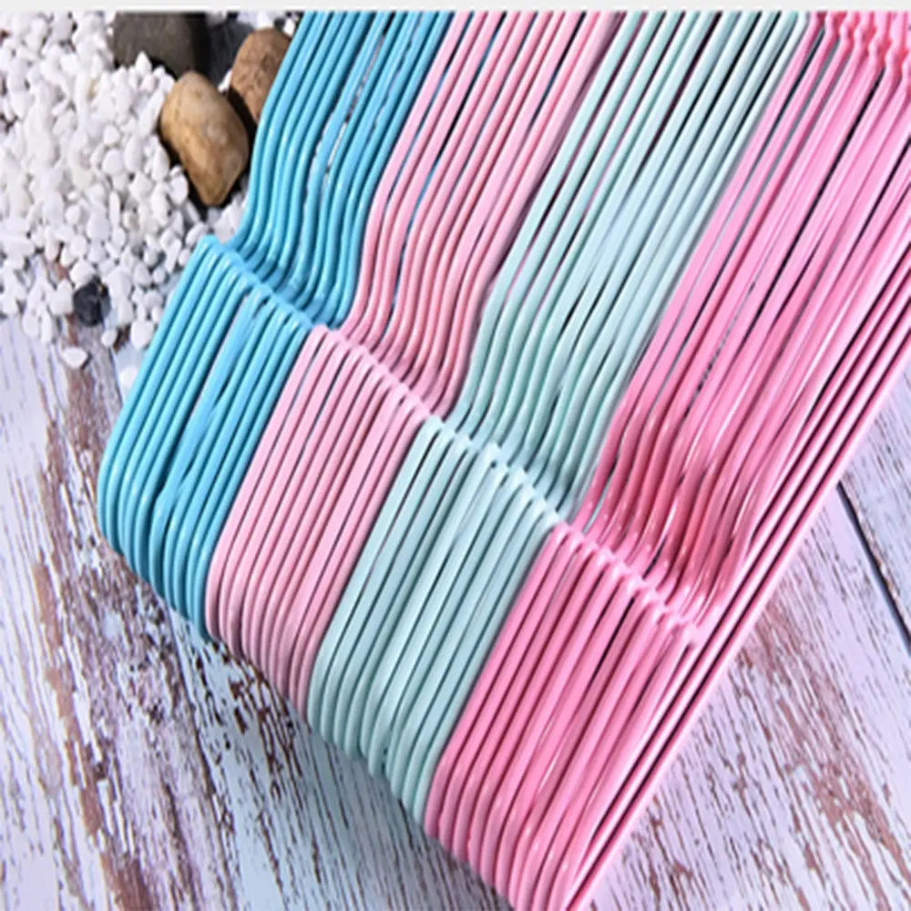 Ganchos para ropa delgados en colores azul, rosado y verde menta, apilados sobre una superficie de madera clara y piedras blancas.